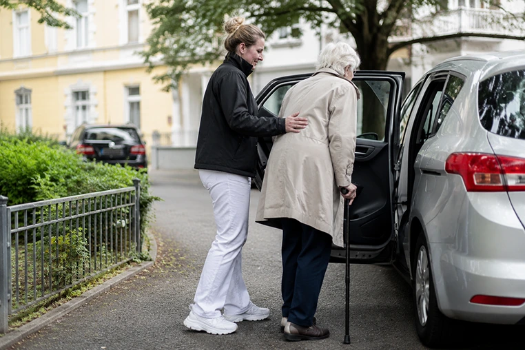 Pflegekraft unterstützt eine ältere Person beim Einsteigen in ein Fahrzeug im ambulanten Pflegedienst.