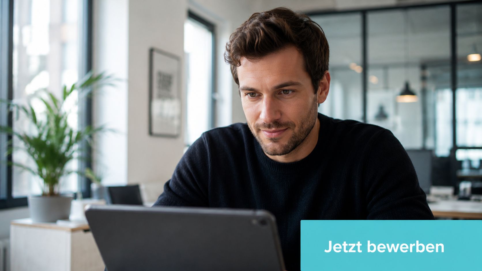 Ein fokussierter Mann sitzt im Büro und arbeitet konzentriert an einem Tablet mit der Aufforderung Jetzt bewerben.
