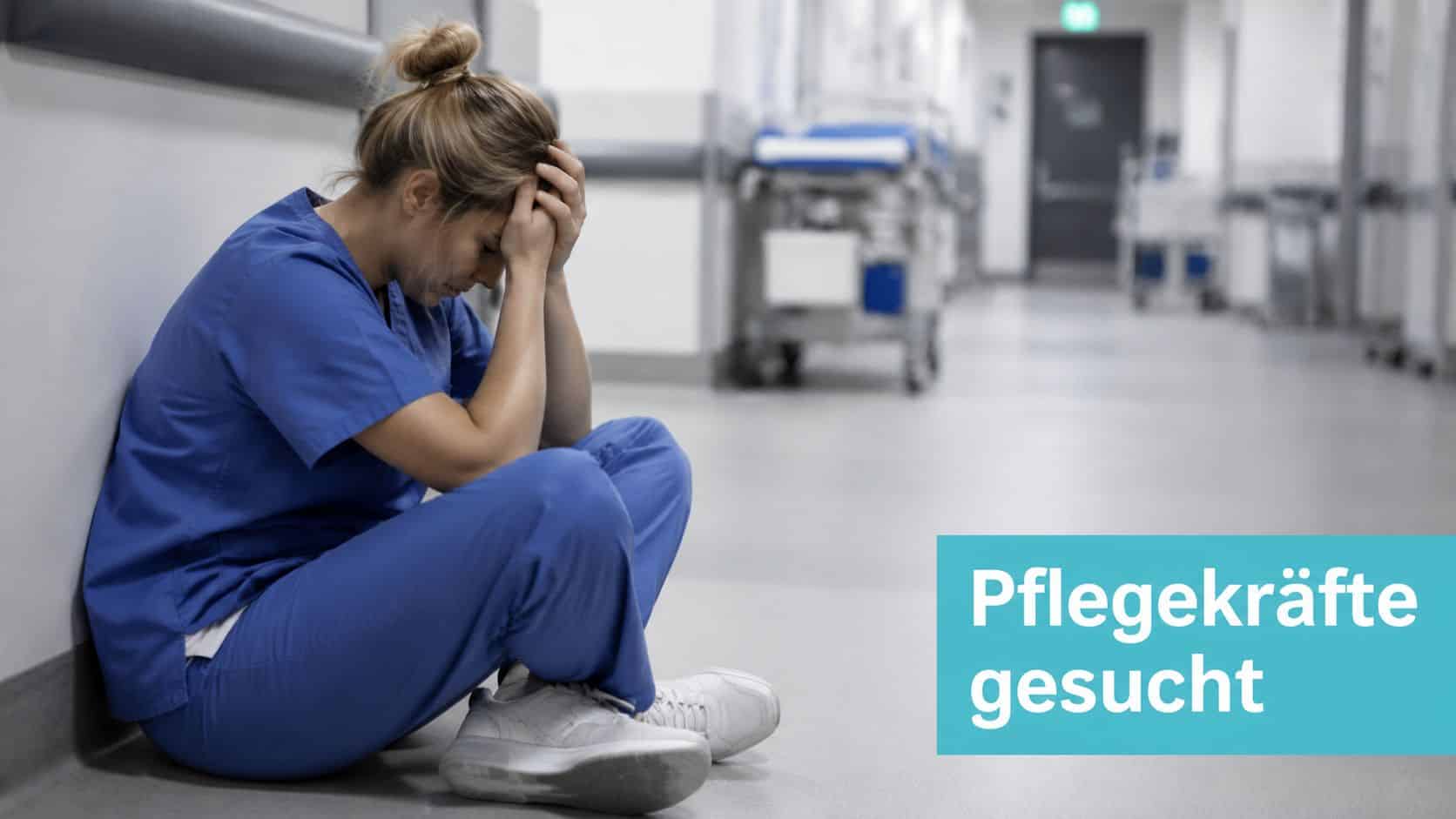 Eine erschöpfte Pflegekraft sitzt mit gesenktem Kopf auf dem Krankenhausboden, im Hintergrund verschwommene Krankenhausgänge.