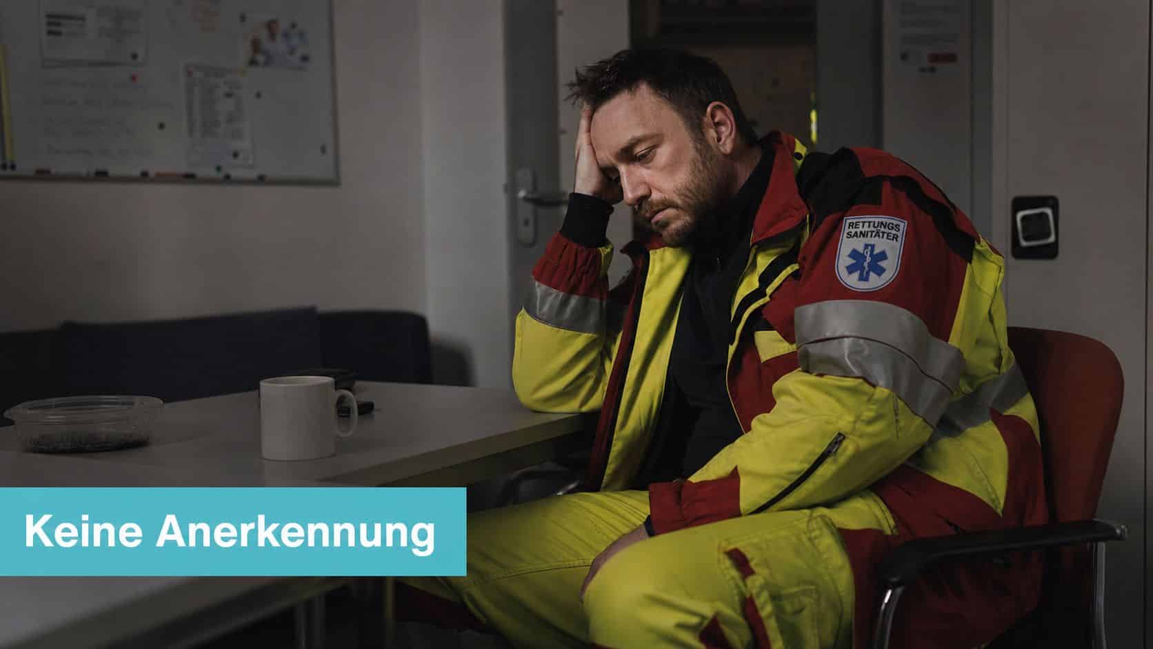 Ein erschöpfter Rettungssanitäter sitzt nachdenklich und deprimiert an einem Tisch in einem Aufenthaltsraum mit der Aufschrift Keine Anerkennung.